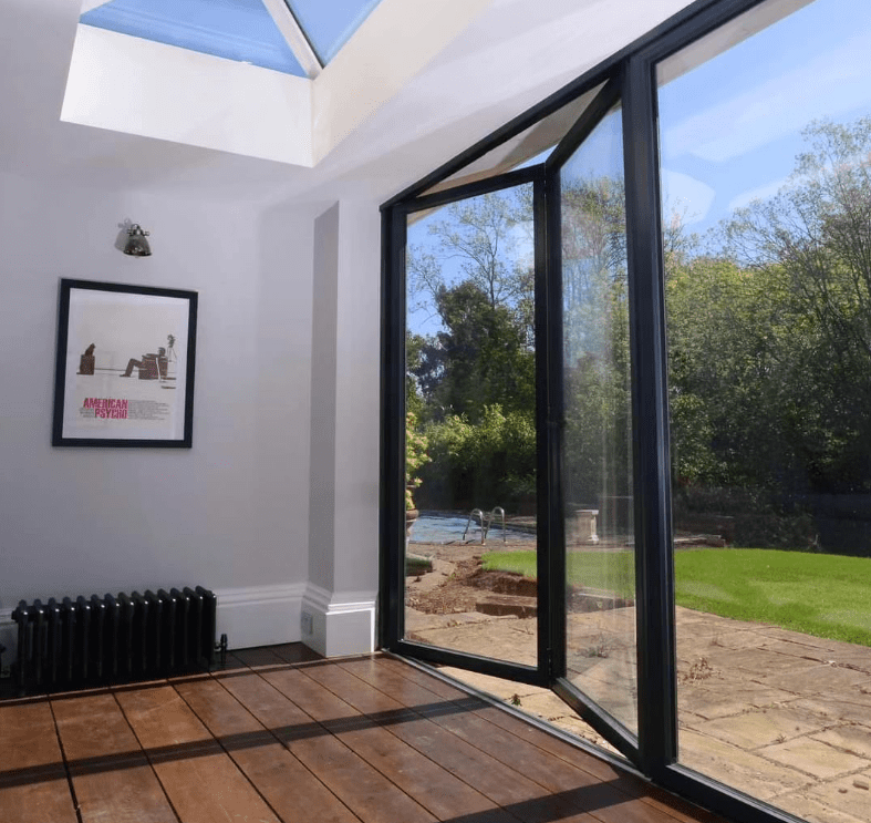 Modern room with a glass roof lantern and black-framed sliding doors opening onto a garden patio.