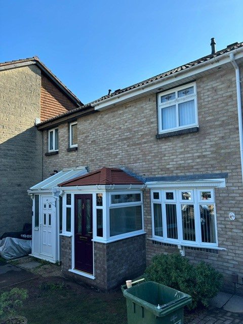 A house with a refurbished porch featuring a tiled red roof, brick base, and a maroon front door with decorative glass.