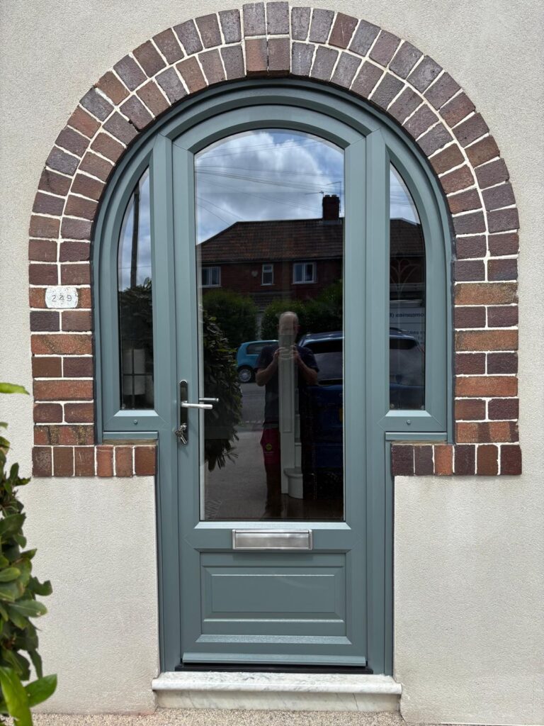 Slate grey arched UPVC front door with full-height glazed panels and chrome handle in brick archway.