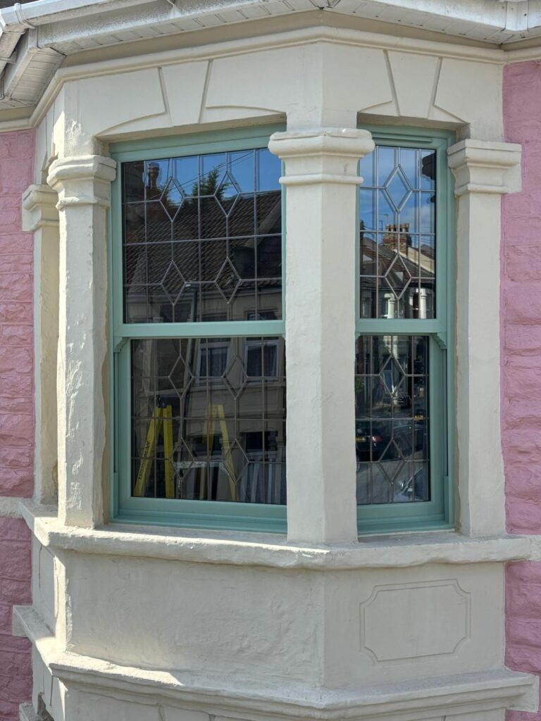 Green decorative glass sash windows of a pink Victorian terraced house, zoomed in to show detail