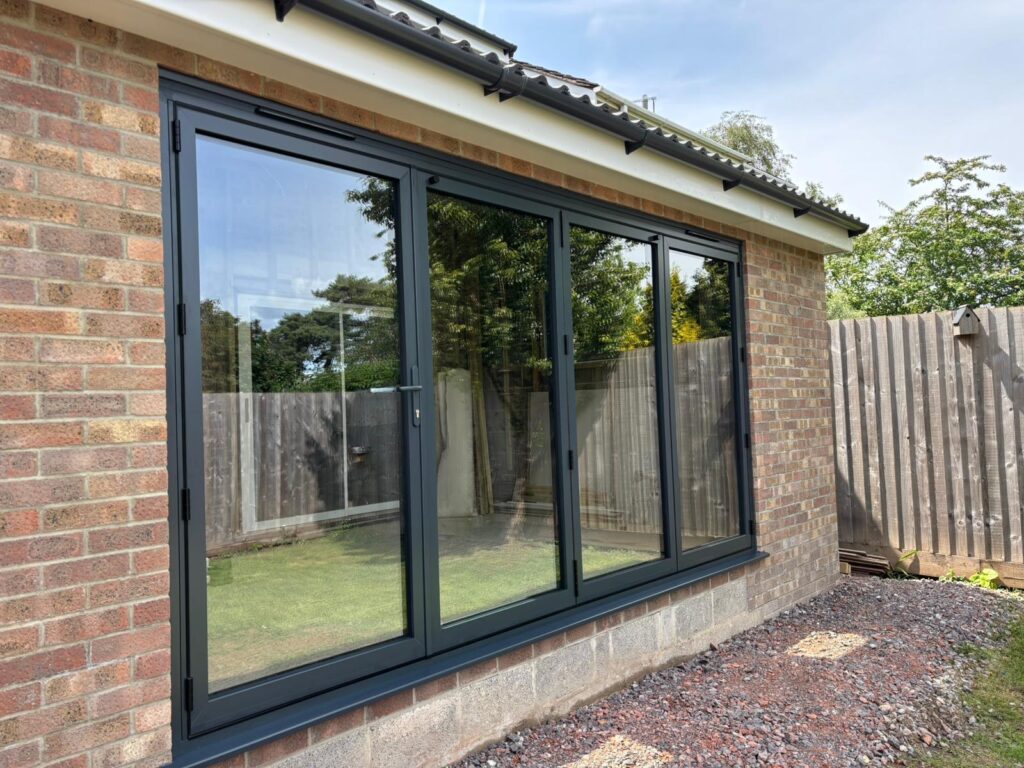 Anthracite grey aluminium patio doors fully closed, reflecting the garden and sky in large glass panels.