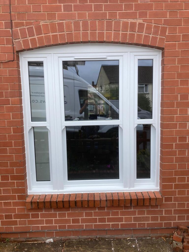 White uPVC triple-panel casement window with arched brick surround on red-brick exterior wall.
